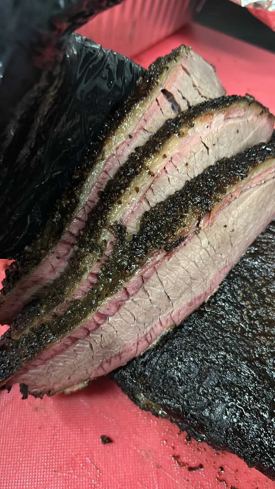 Sliced smoked brisket with a peppery bark on a red cutting board