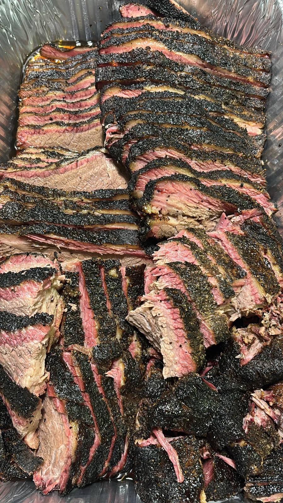 A full pan of sliced smoked brisket with a heavy black bark