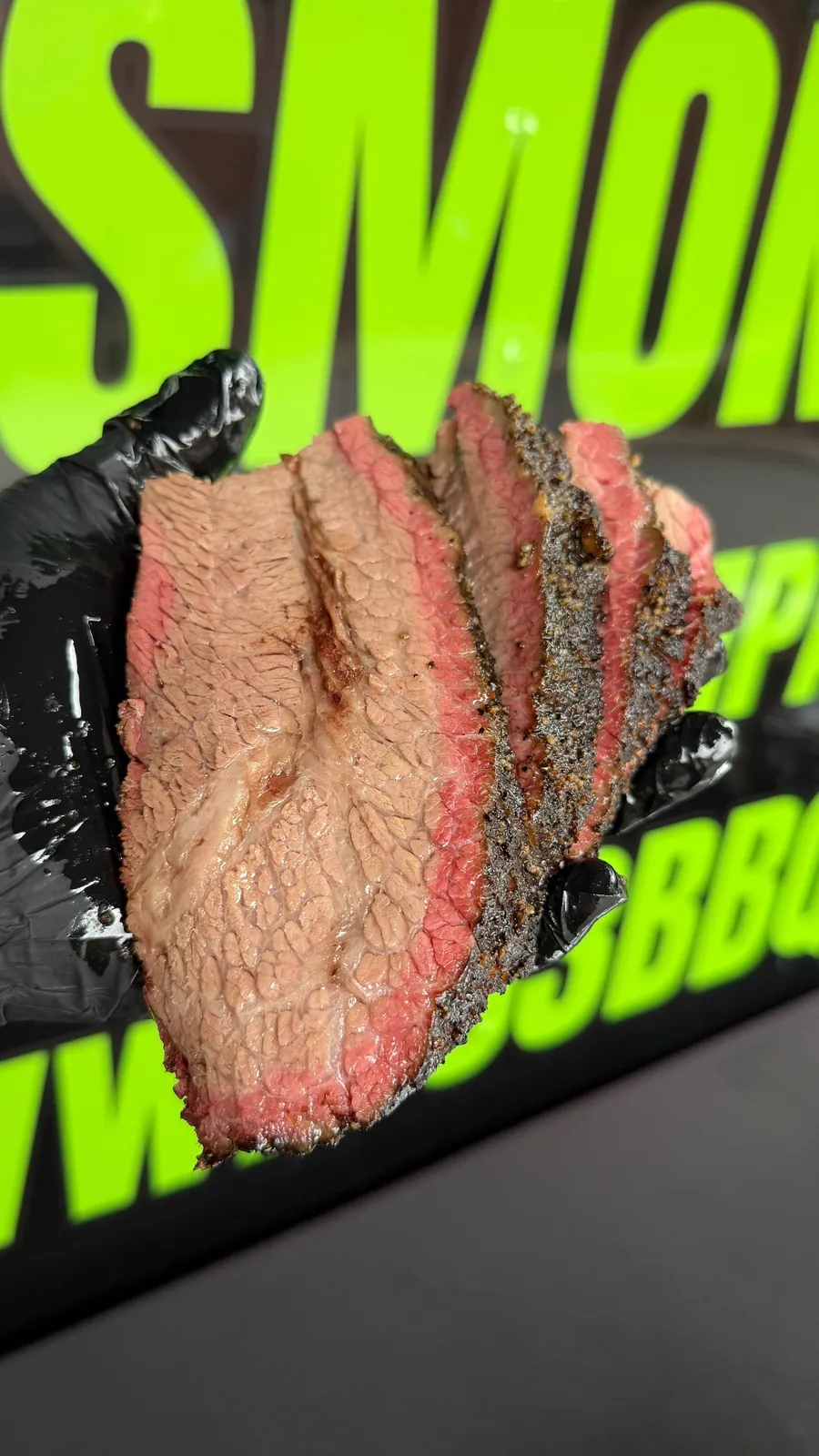 Sliced smoked brisket held in a black glove in front of the trailer lettering