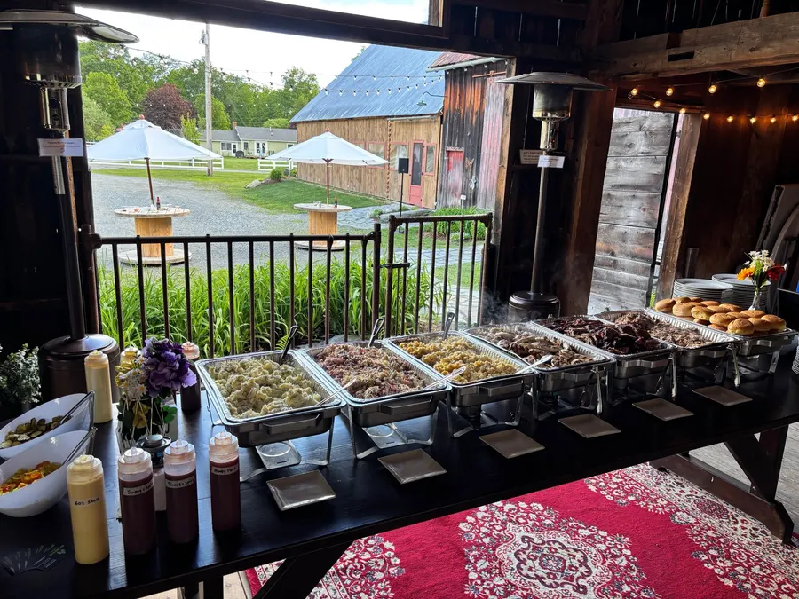 A full BBQ buffet line set up in a barn, with sauce bottles at the front