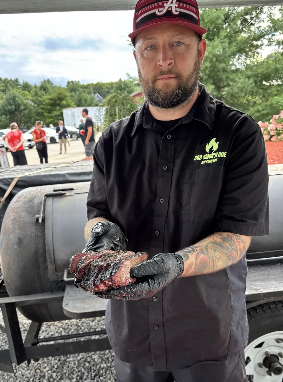 Josh Hilyard holding sliced brisket in front of his smoker