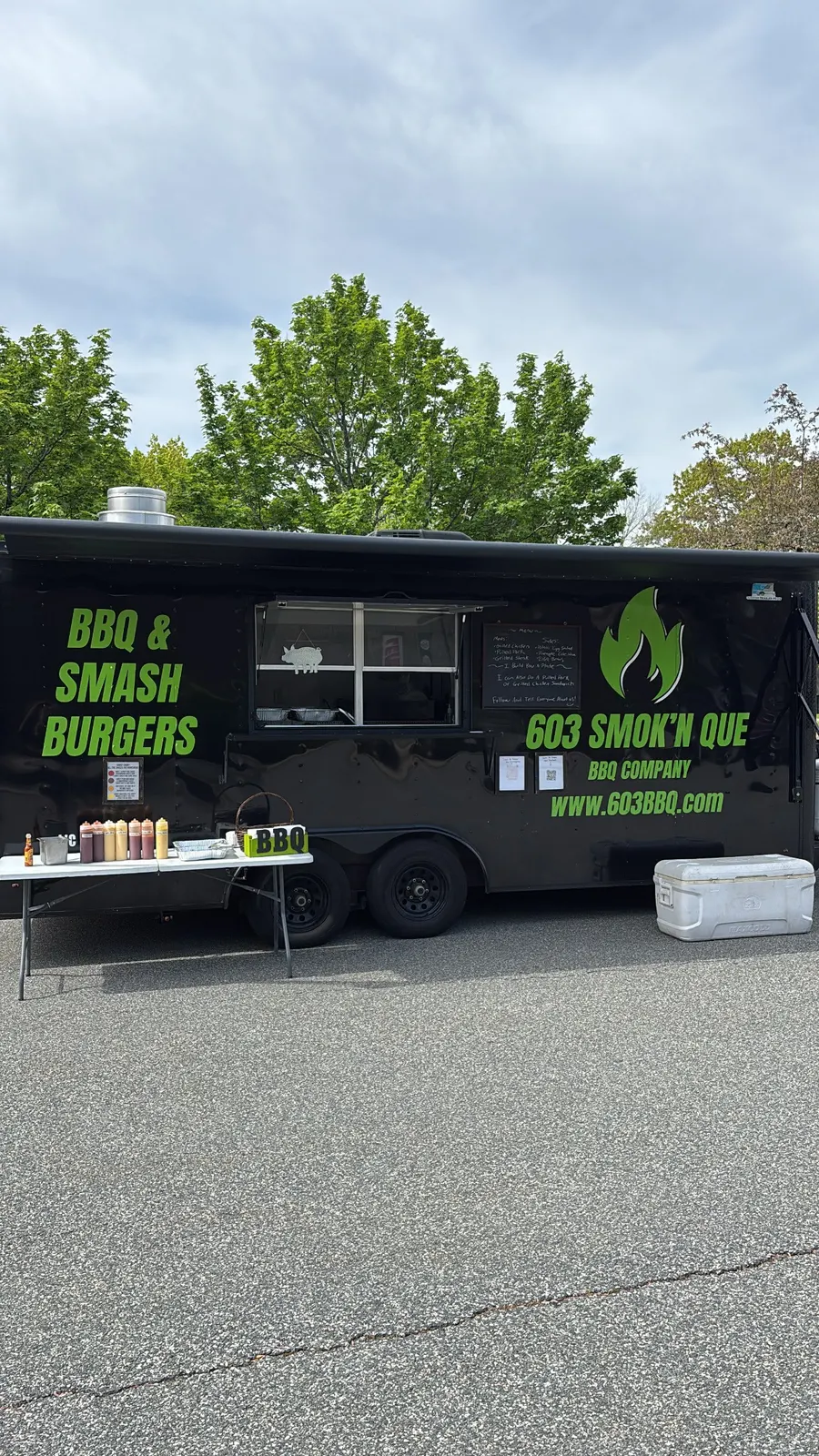 The black 603 Smok'n Que trailer with BBQ and Smash Burgers lettered on the side